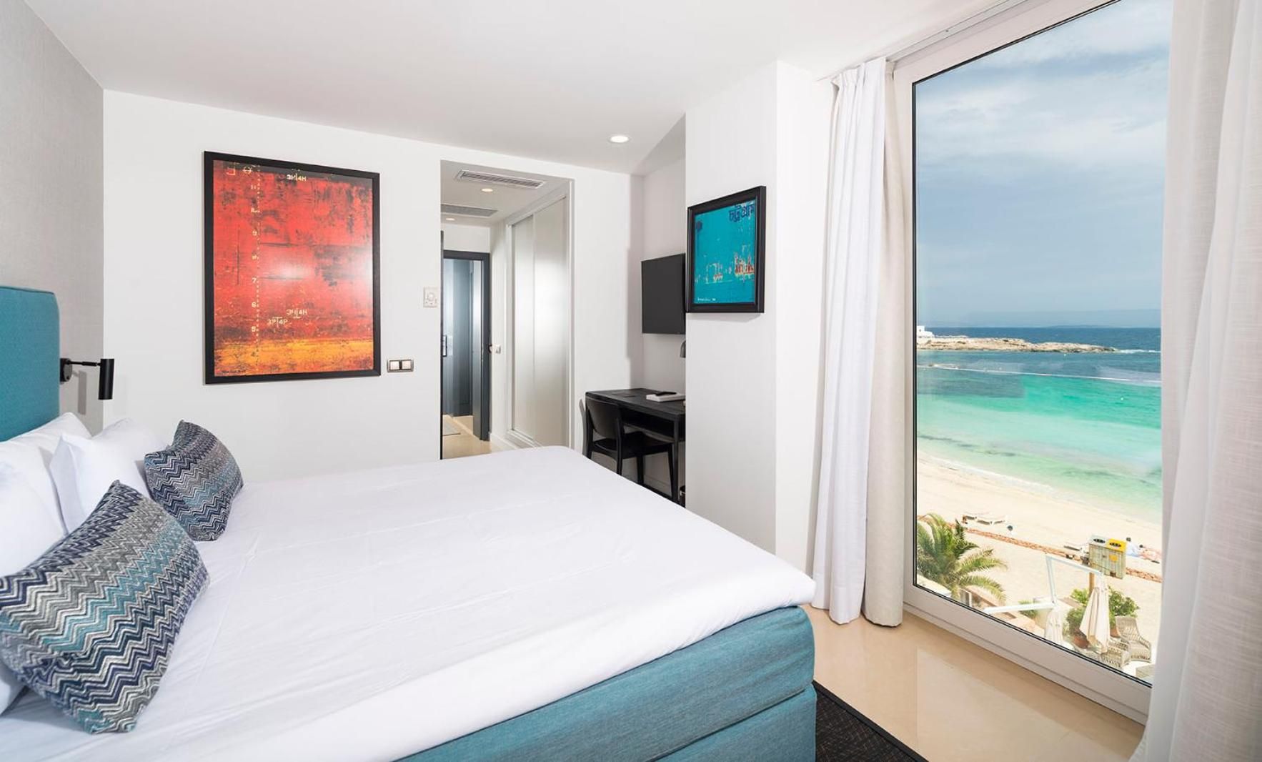 Ein Hotelzimmer mit Bett, Schreibtisch und großem Fenster mit Blick auf den Strand.