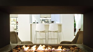 A modern outdoor seating area with a fire feature, two white chairs, and a kitchen in the background. - Tahiti (Formentera)