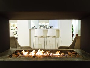 A modern outdoor seating area with a fire feature, two white chairs, and a kitchen in the background. - Tahiti (Formentera)