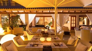 An outdoor dining area with wicker furniture, a wooden table, and ambient lighting. - Tahiti (Formentera)