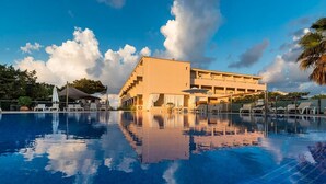 A swimming pool with lounge chairs and umbrellas, a building with a flat roof, and a clear sky with clouds. - Tahiti (Formentera)