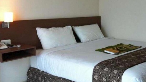 A hotel room with a bed, a nightstand with a lamp, and a framed picture on the wall. - Bunda Hotel Bukittinggi (Bukittinggi)