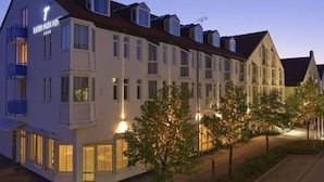 A multi-story hotel with a traditional European architectural style, featuring a prominent entrance with a sign. - Dormero Hotel München-kirchheim Messe (Kirchheim by Munich)