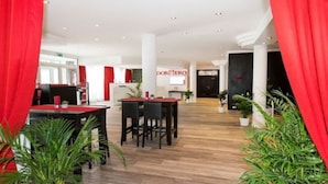 A modern hotel lobby with a reception desk, red curtains, and potted plants. - Dormero Hotel München-kirchheim Messe (Kirchheim by Munich)