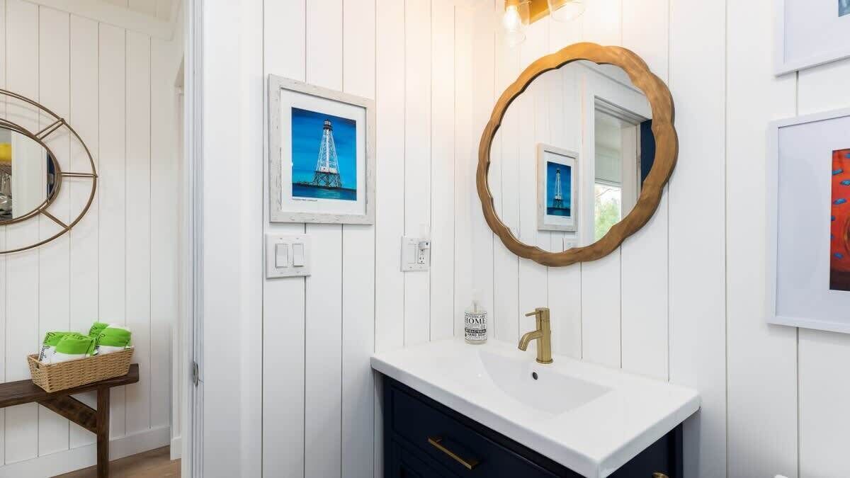 Een badkamer met een witte wastafel, een gouden kraan, een spiegel met houten lijst en ingelijste foto's aan de muur.
