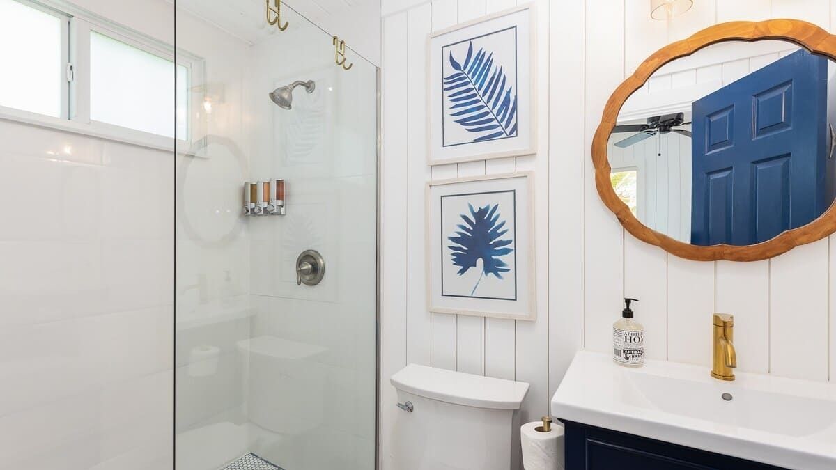 A bathroom with a glass shower enclosure, a white sink with a gold faucet, and framed leaf artwork on the wall.