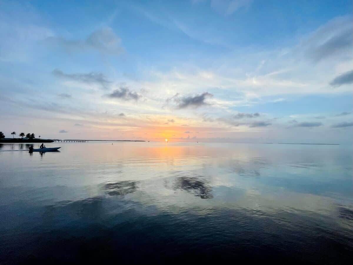 Un plan d'eau paisible, avec un coucher de soleil, une jetée et un petit bateau.