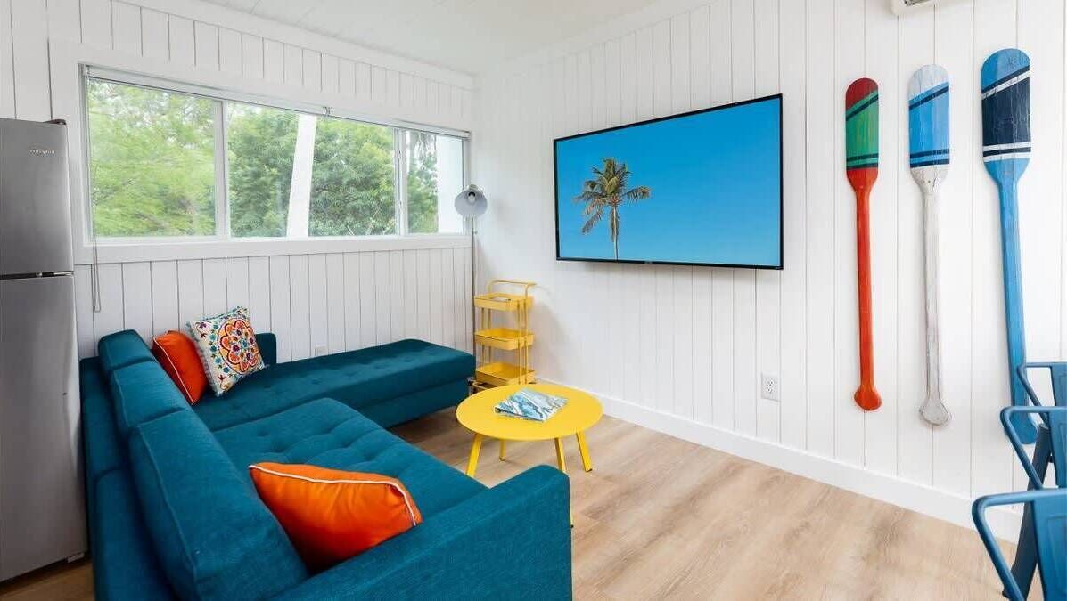 Una sala de estar moderna con un sofá azul verdoso, una mesita amarilla, un televisor y una tabla de remo fijada a la pared.