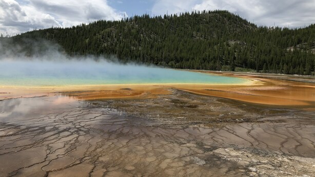 A geothermal area with a lake, forested hill, and steam rising from the ground. - Yellowstone Retreat Rentals U2: two blocks from Yellowstone! (Gardiner)
