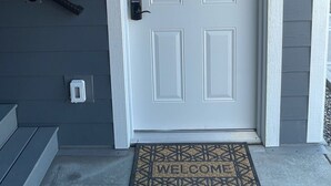 A white door with a keypad lock, a number '2' sign above it, a metal doorbell, and a welcome mat at the entrance. - Yellowstone Retreat Rentals U2: two blocks from Yellowstone! (Gardiner)