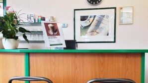 A reception desk with a green counter, a clock, a framed picture, and a potted plant. - Motel Frankfurt by Advena (Frankfurt)
