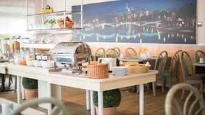 A restaurant with a buffet setup, including a self-service station with various food items and a large cityscape mural on the wall. - Motel Frankfurt by Advena (Frankfurt)
