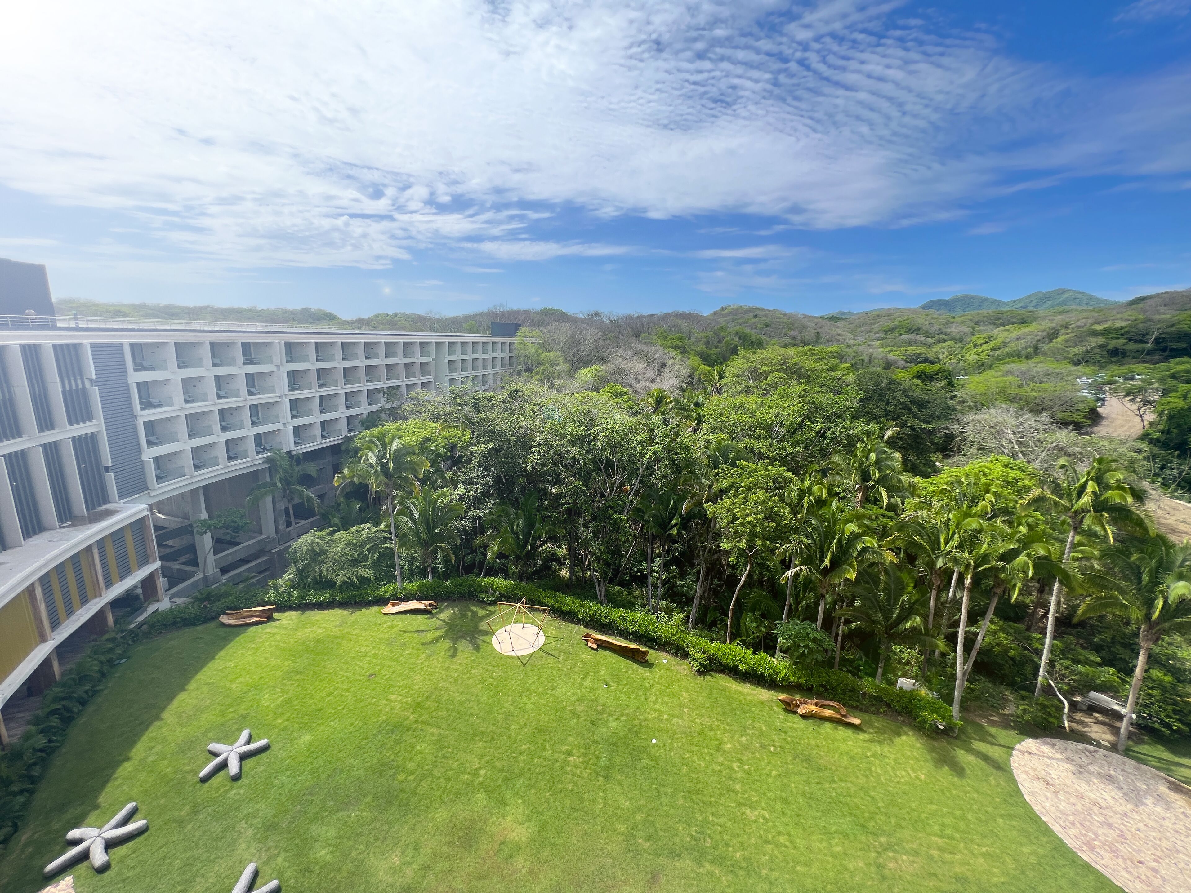 A hotel courtyard with a lawn, palm trees, and a view of a mountainous landscape.