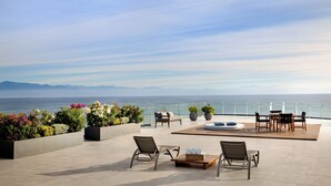 Una terraza en la azotea con mobiliario exterior, plantas en macetas y vistas al mar.