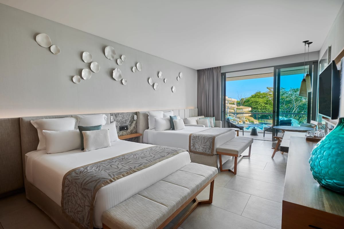 A modern hotel room with two beds, a seating area, and a balcony with a pool view.