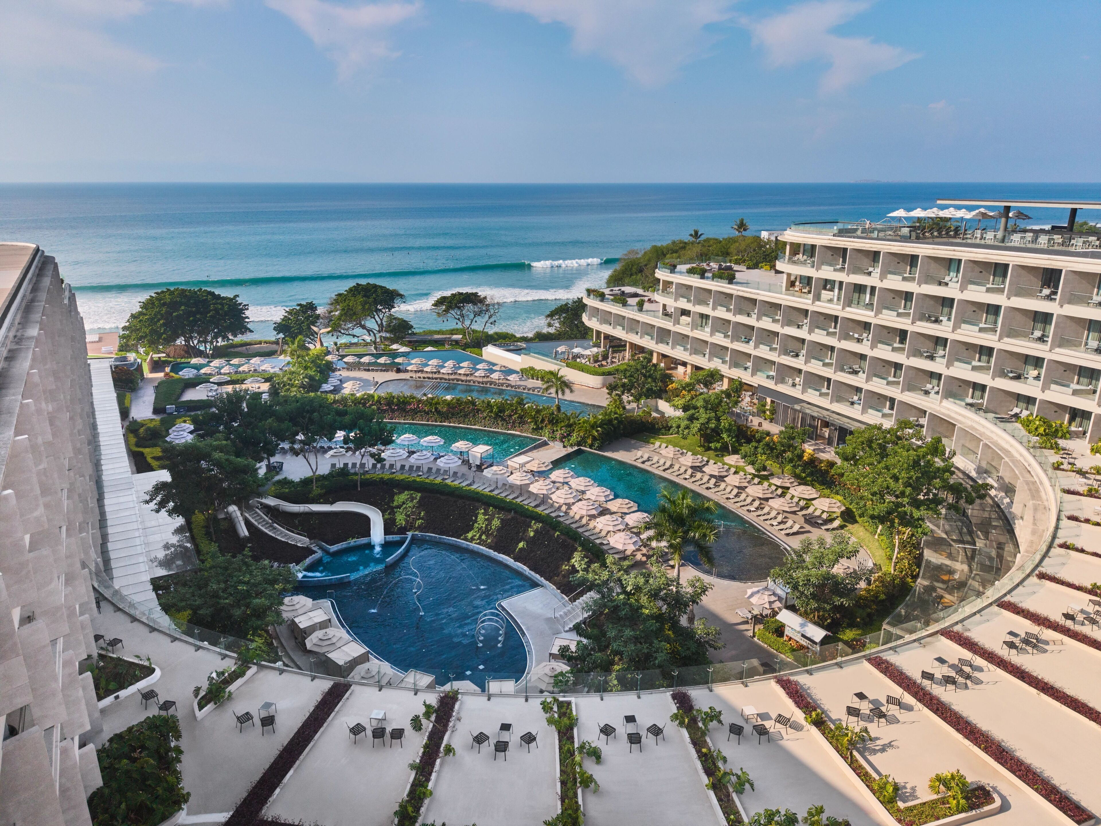 A resort with a pool, lounge chairs, and a view of the ocean.