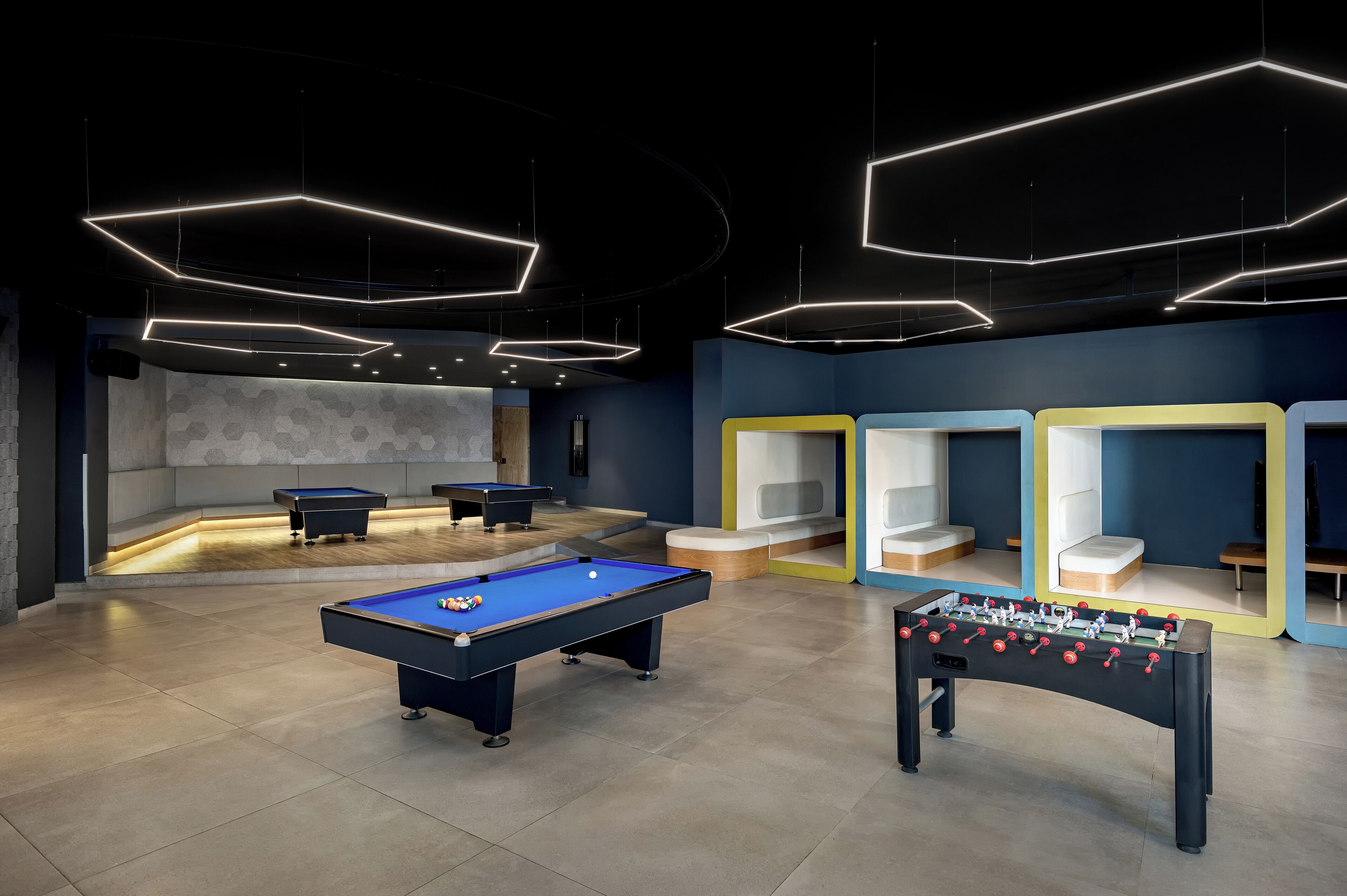 A modern indoor recreational area with pool tables, a foosball table, and geometric ceiling lights.