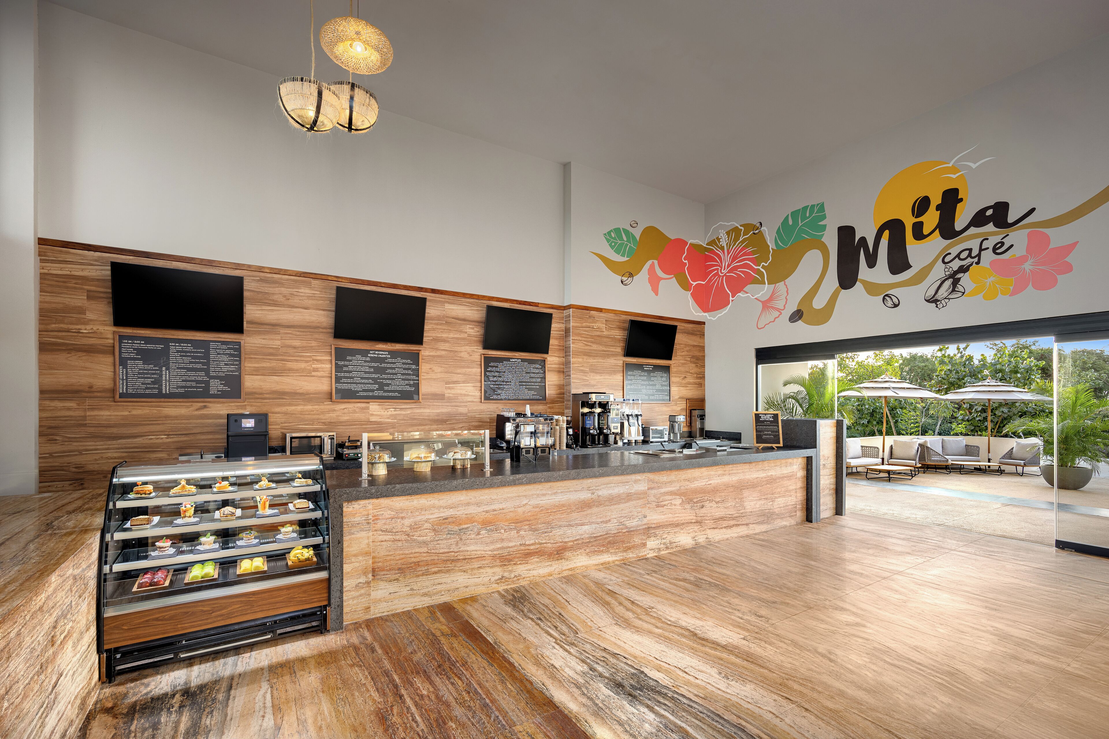 L’intérieur d’un café moderne, avec un comptoir en bois, des panneaux affichant le menu et un espace salon agrémenté de parasols.