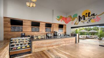 L’intérieur d’un café moderne, avec un comptoir en bois, des panneaux affichant le menu et un espace salon agrémenté de parasols.