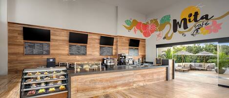 A modern cafe interior with a wooden counter, menu boards, and a seating area with umbrellas.