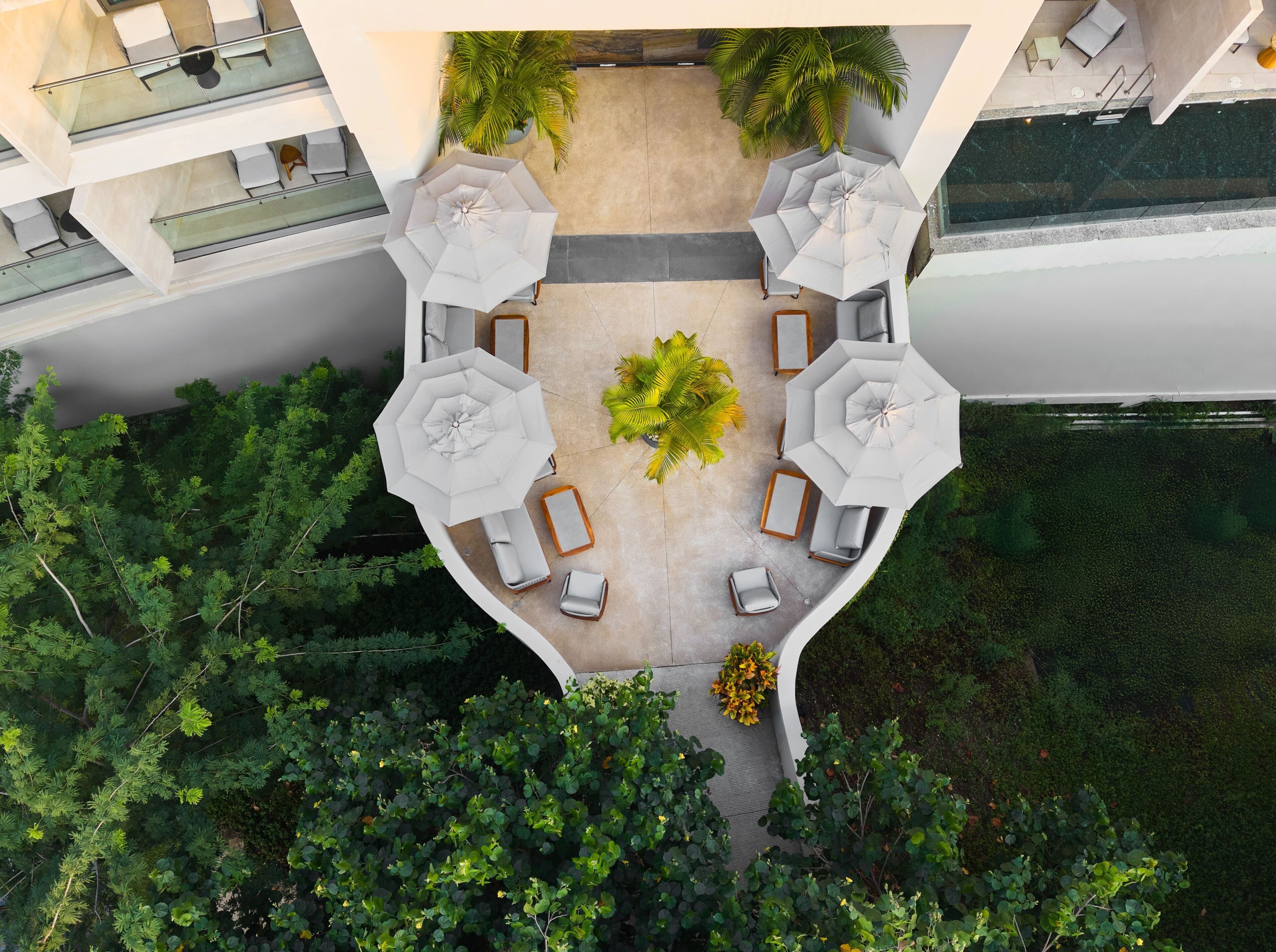 Vista aérea de um terraço com mobiliário ao ar livre, guarda-sóis e vegetação ao redor.