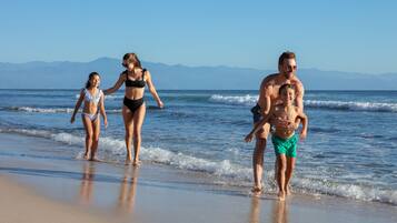 Una familia caminando en la playa con montañas al fondo.