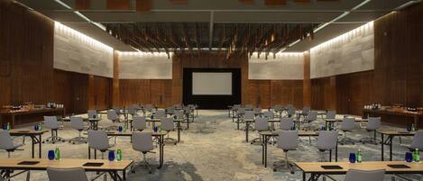 A conference room with rows of tables and chairs, a large screen at the front, and wooden paneling on the walls.