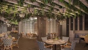 Un restaurante con mesas redondas, sillas estampadas, plantas colgantes e iluminación colgante.