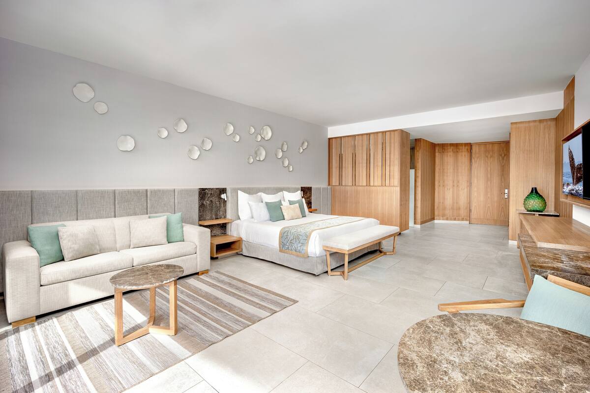 A modern hotel room with a bed, sofa, and a dining area.