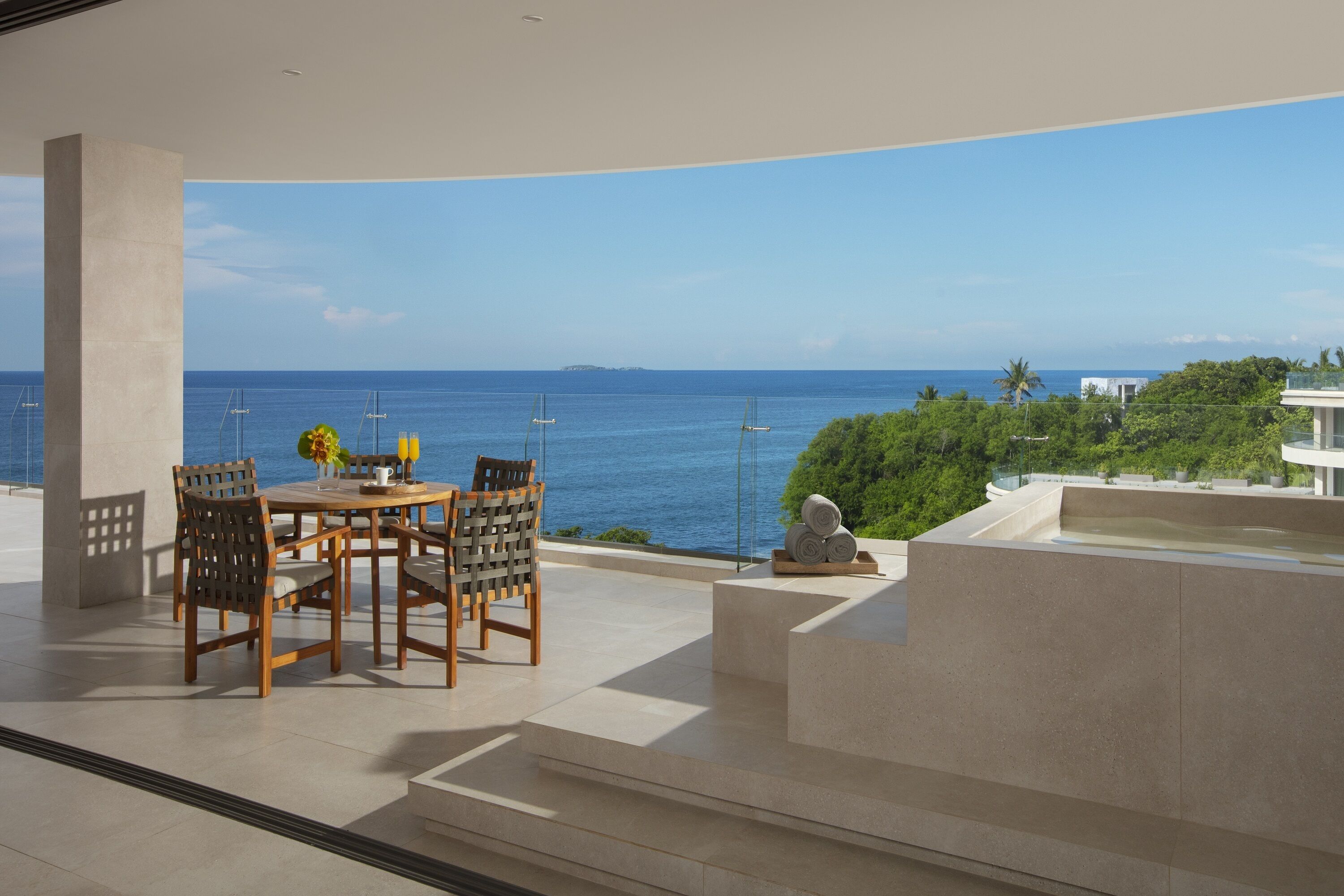 A modern outdoor dining area with a view of the sea, featuring a table and chairs, a small garden, and a water feature.