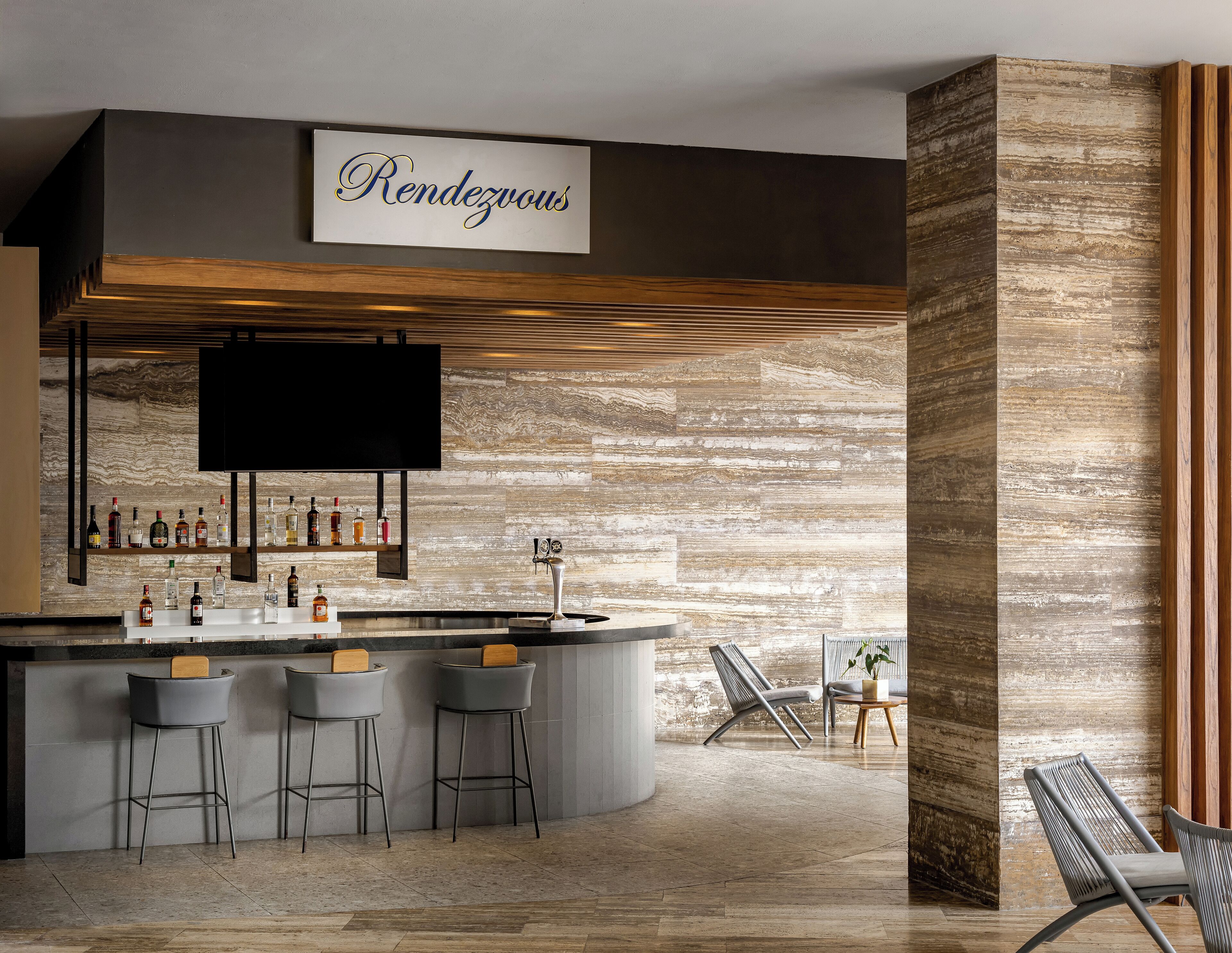 A bar area with a sign reading "Rendezvous," bar stools, a TV, and a variety of bottles.
