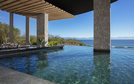 An infinity pool with clear water, a wooden pergola, and a view of the ocean.