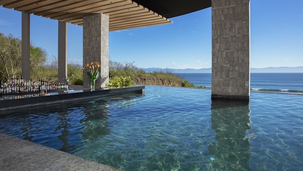 Una piscina infinita con agua cristalina, una pérgola de madera y vista al océano.