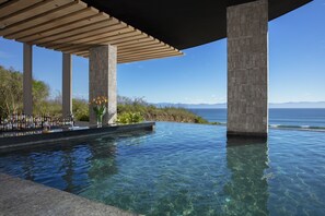 Una piscina infinita con agua cristalina, una pérgola de madera y vista al océano.