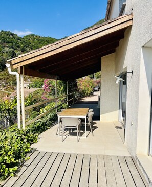 Un patio exterior con mesa y sillas de madera, una pérgola y vistas a una colina.