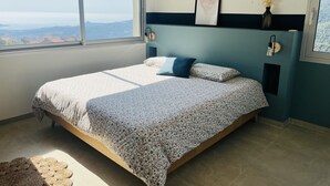 A bedroom with a bed, a view of the outdoors, a framed picture on the wall, and a vase with dried flowers. - Charming house with sea and mountain views and private pool (Sari-d'Orcino)