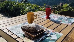 A wooden table with a floral placemat, a yellow mug, a red mug, a plate with a pastry, and a spoon. - Charming house with sea and mountain views and private pool (Sari-d'Orcino)