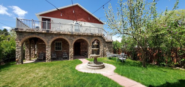 Une maison en pierre à deux étages, dotée d’un balcon, d’une entrée en arc de pierre et d’une fontaine dans la cour.
