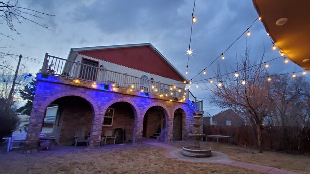 A building with a red roof, stone arches, and a balcony with string lights. - Western Carriage House Studio Suite- Western themed retreat- Full Kitchen & Bath (Gillette)