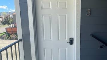 A white door with a welcome mat, a mailbox, and a number '3' sign on a gray house.