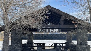Un pabellón de piedra con un letrero que dice "ARCH PARK" y mesas de picnic.