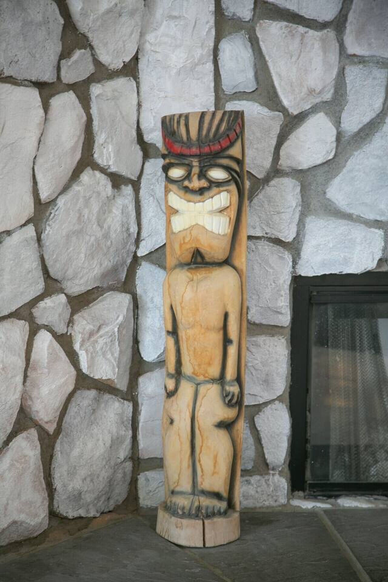 A wooden totem with a carved face, standing against a stone wall.