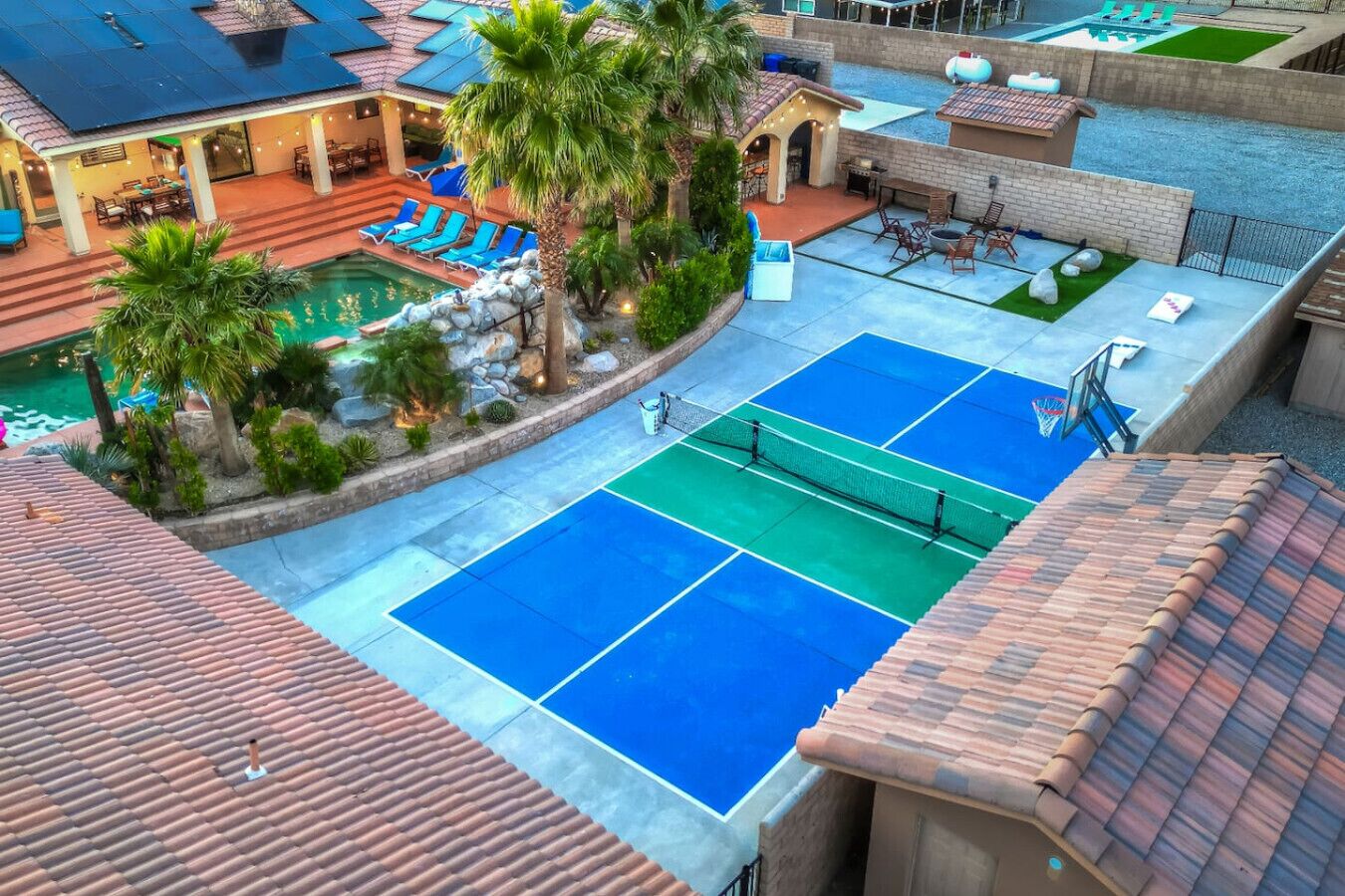 A rooftop pool area with a tennis court, lounge chairs, and a small basketball court.