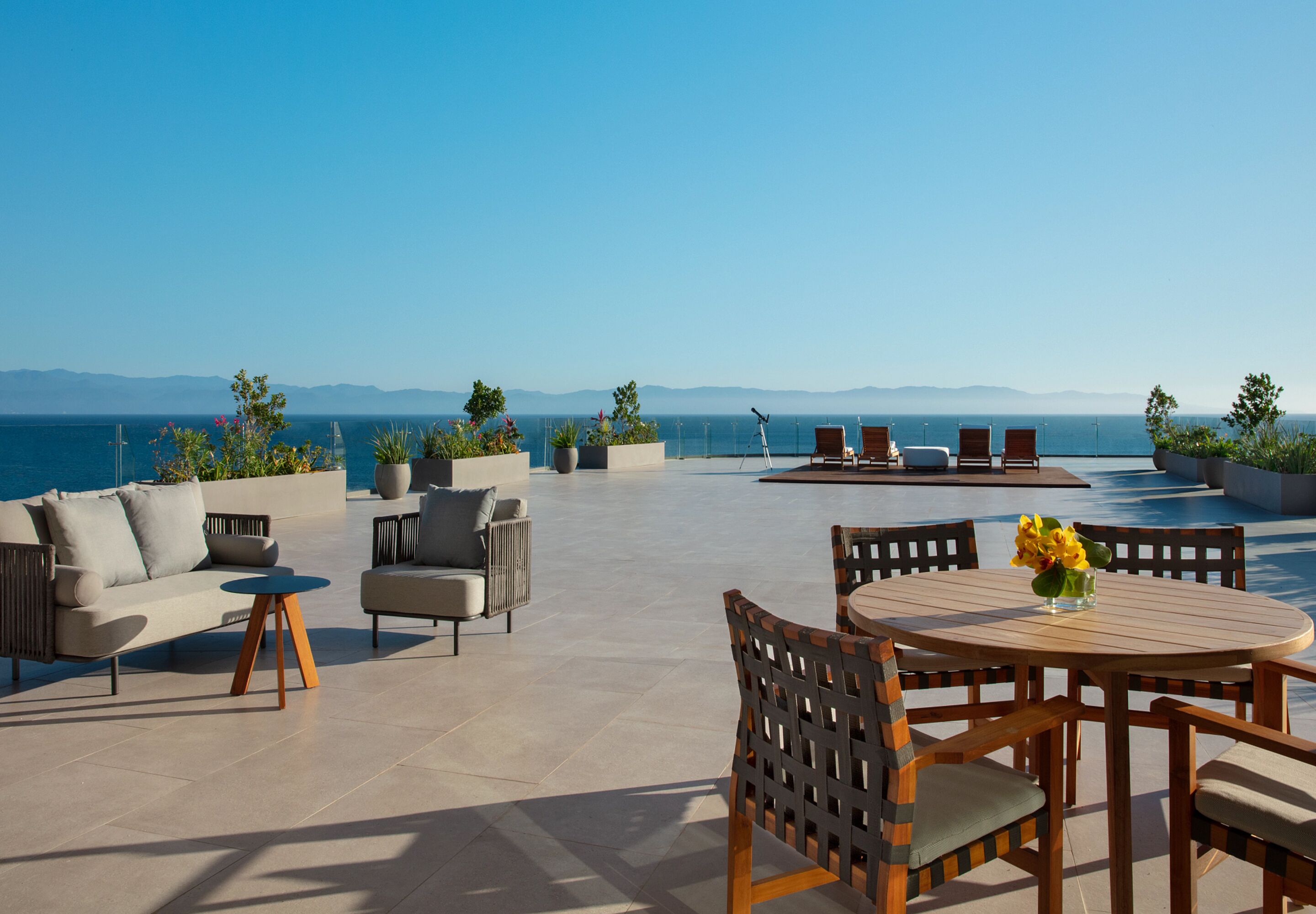 Una terraza en la azotea con mobiliario exterior, piscina y vistas al mar y a las montañas.