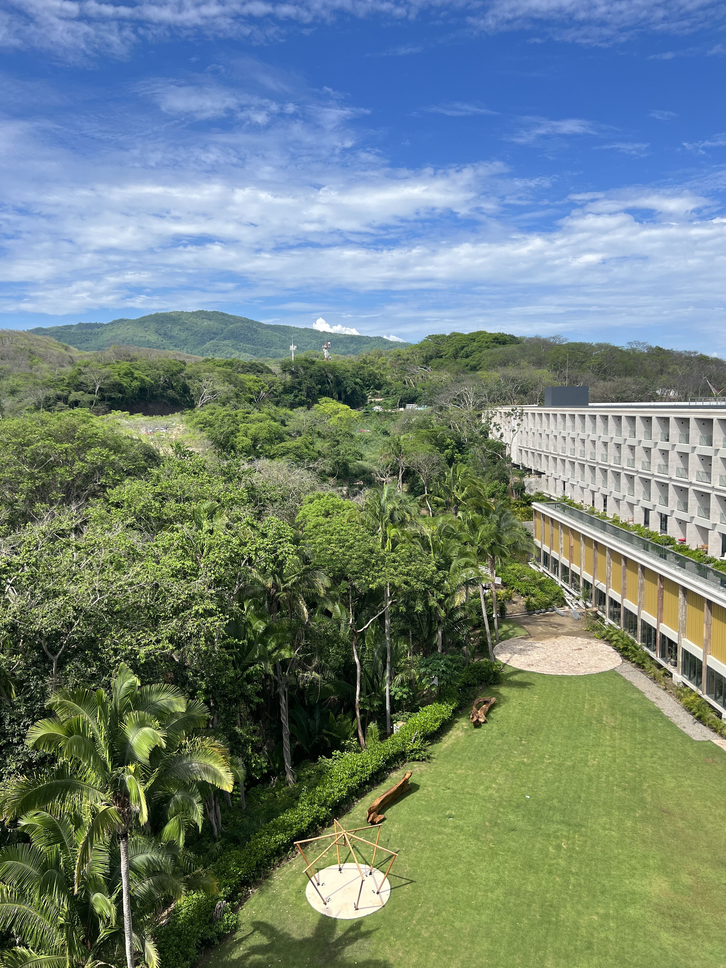 Un hotel con un amplio césped, palmeras y vistas a la montaña.