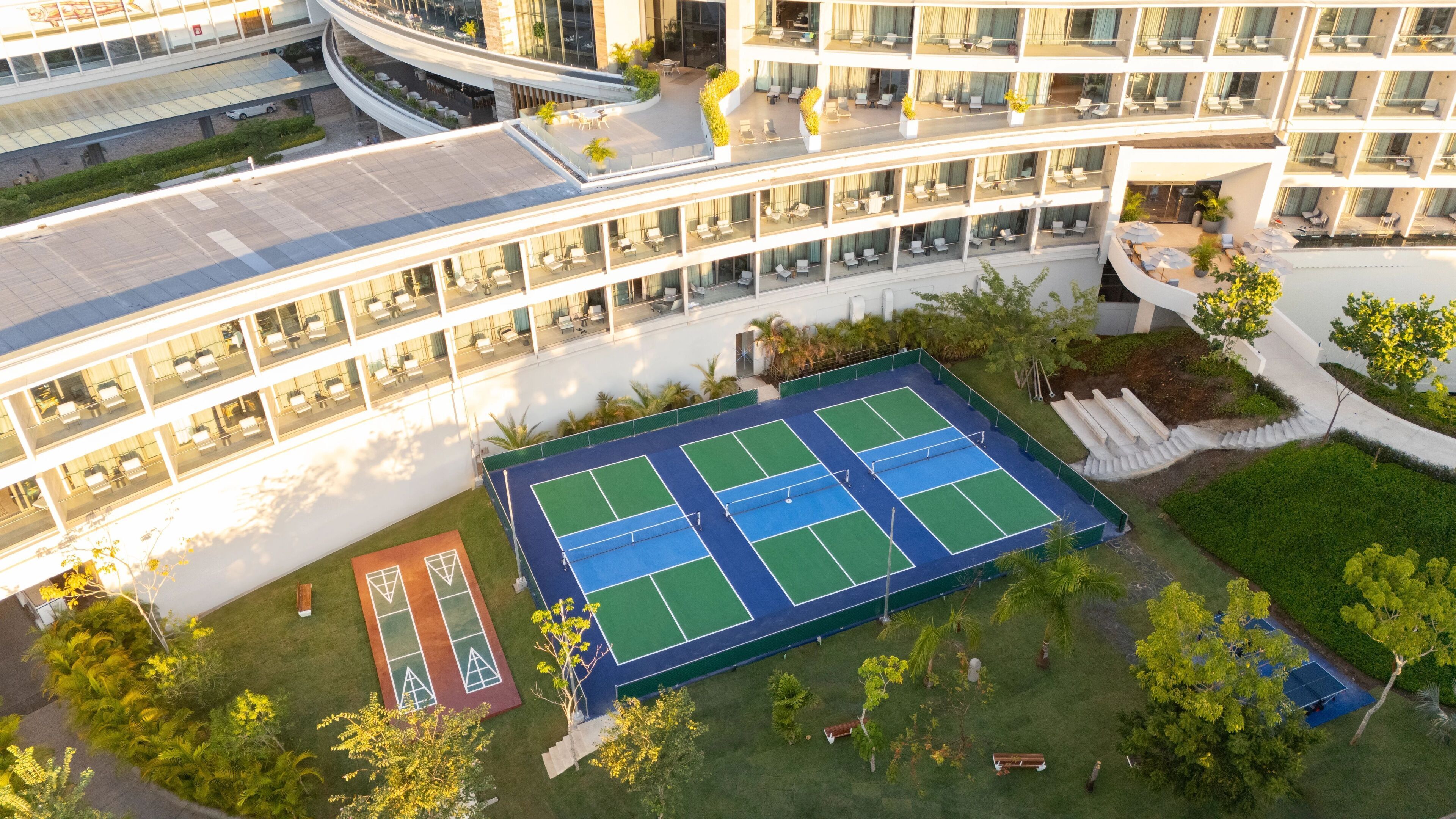A multi-story hotel with a tennis court, outdoor seating, and a curved walkway.