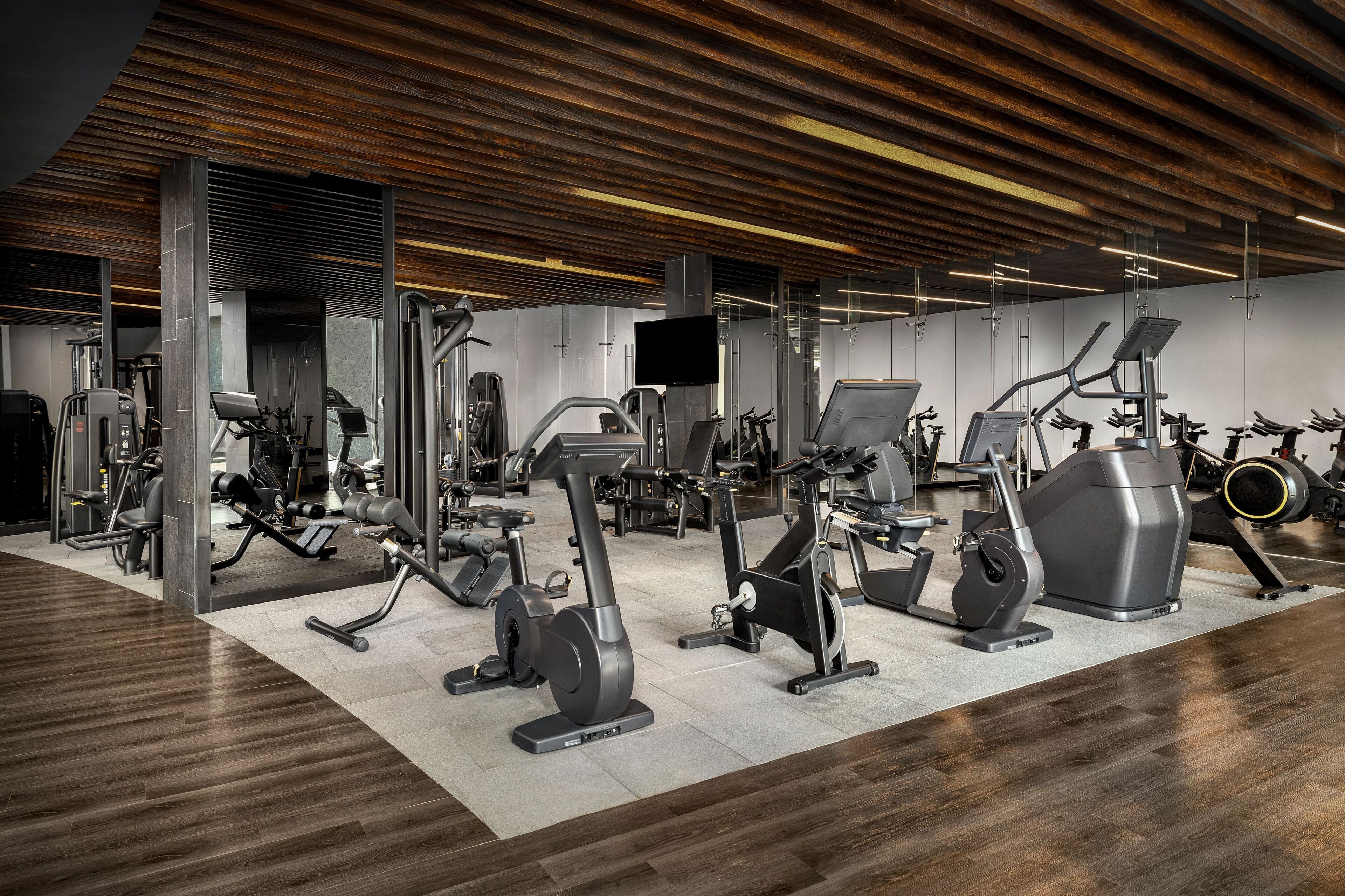 Un gimnasio moderno con diversos equipos de ejercicio, techo de madera y suelo de baldosas.