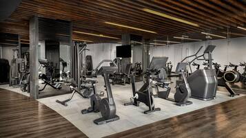 Un gimnasio moderno con diversos equipos de ejercicio, techo de madera y suelo de baldosas.