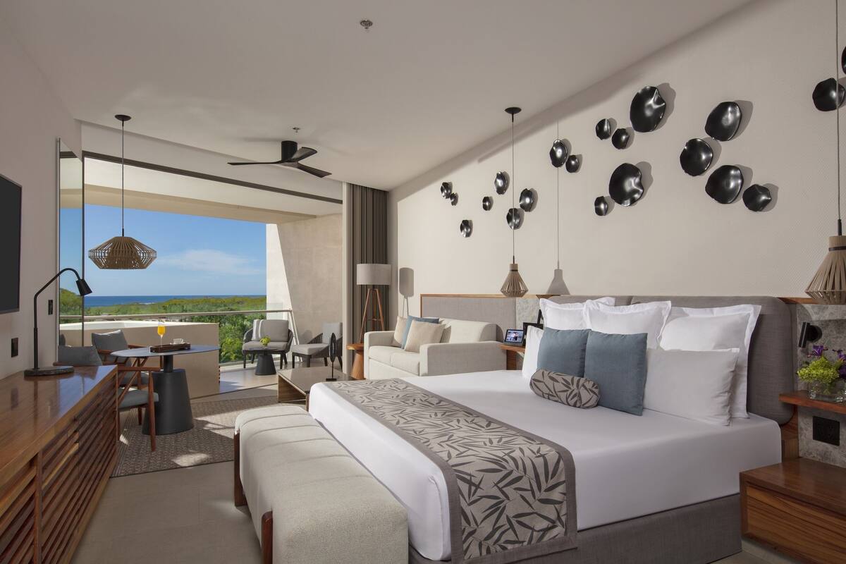Una habitación de hotel moderna con una cama grande, un escritorio y un balcón con vistas al océano.