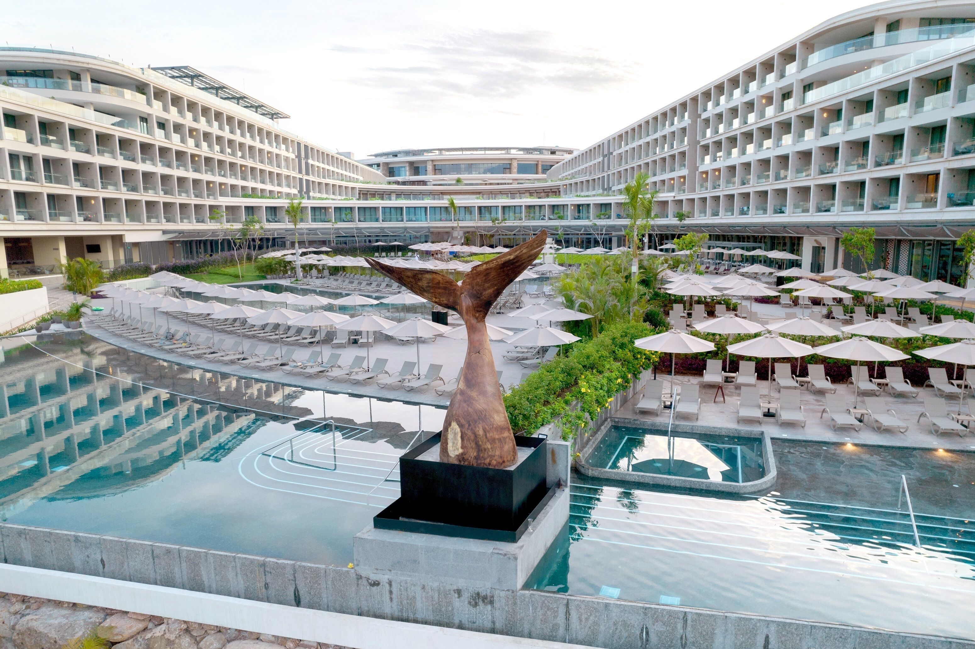 A modern hotel with multiple swimming pools, lounge areas, and a distinctive whale tail sculpture.